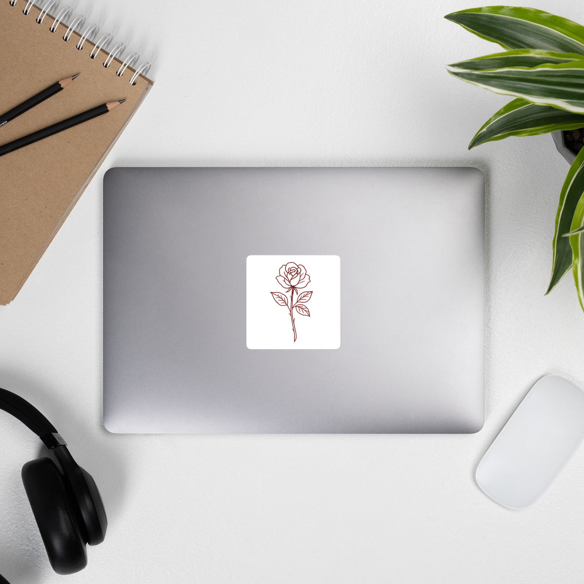 Rose Sticker by By Tee, on a laptop beside headphones and a plant