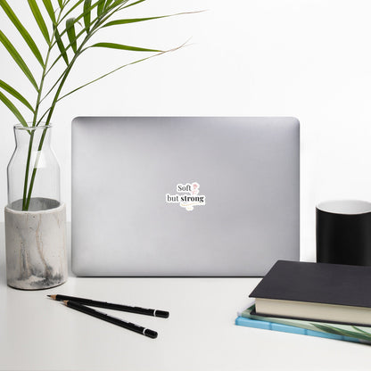 Soft but Strong Sticker by By Tee, on a laptop in a neutral workspace with greenery
