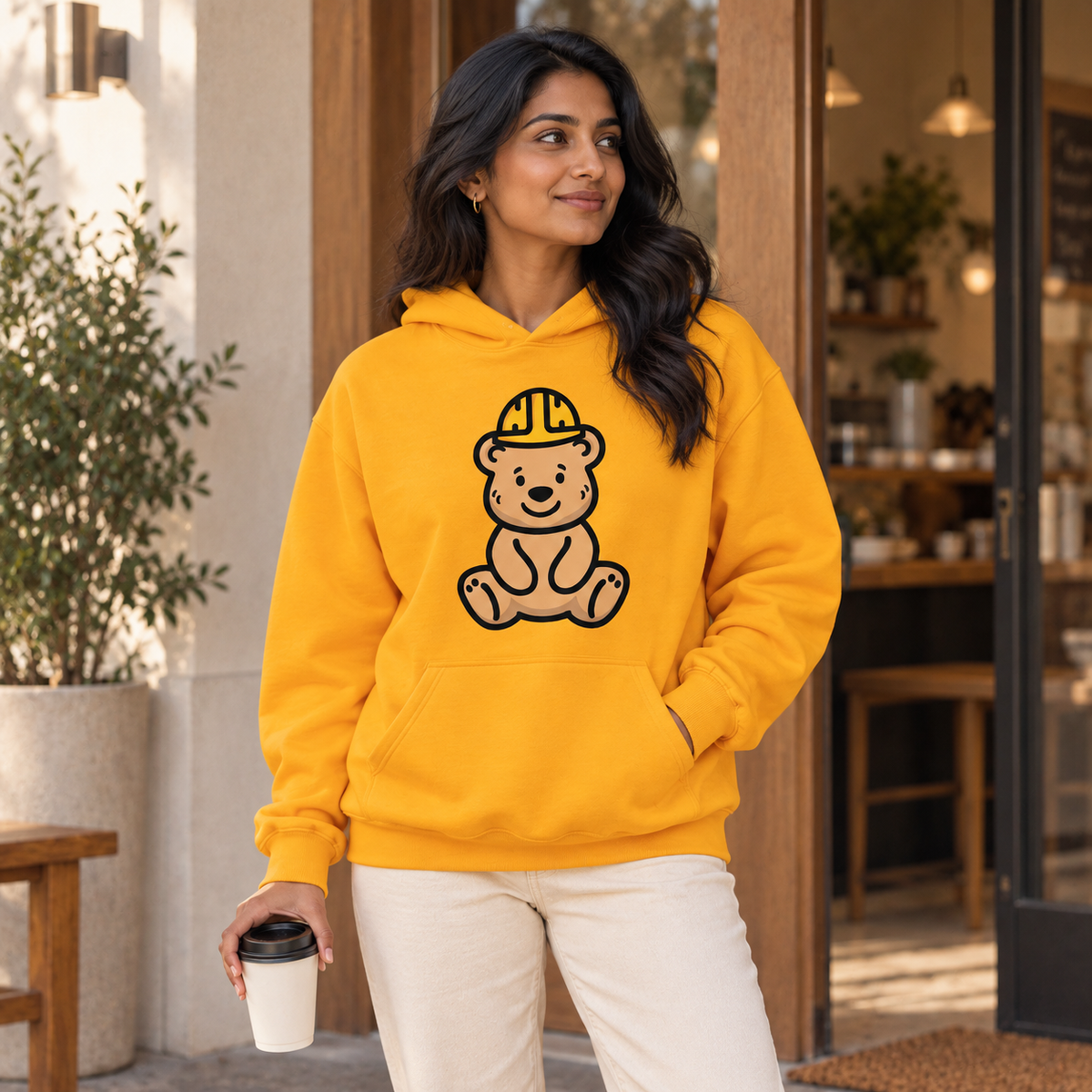 Golden Bear Hug Hoodie — cafe lifestyle mockup.