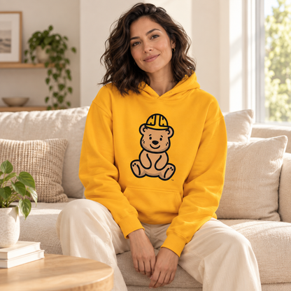 Woman wearing the Golden Bear Hug Hoodie on a cream sofa, with Tee Bear artwork visible.