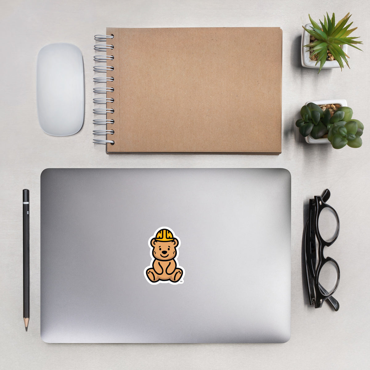 Tee Bear Sticker by By Tee, on a laptop beside a kraft notebook and succulents